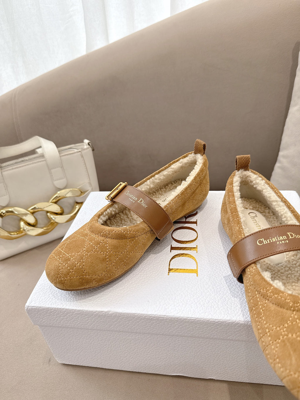 Tan suede slip-on flats with buckled strap and cream shearling lining, on box
