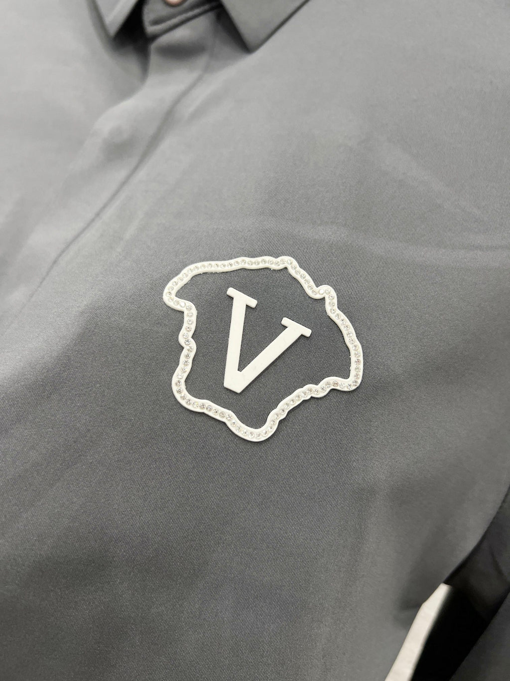 Versace chest crest patch with V emblem on grey button-up shirt.