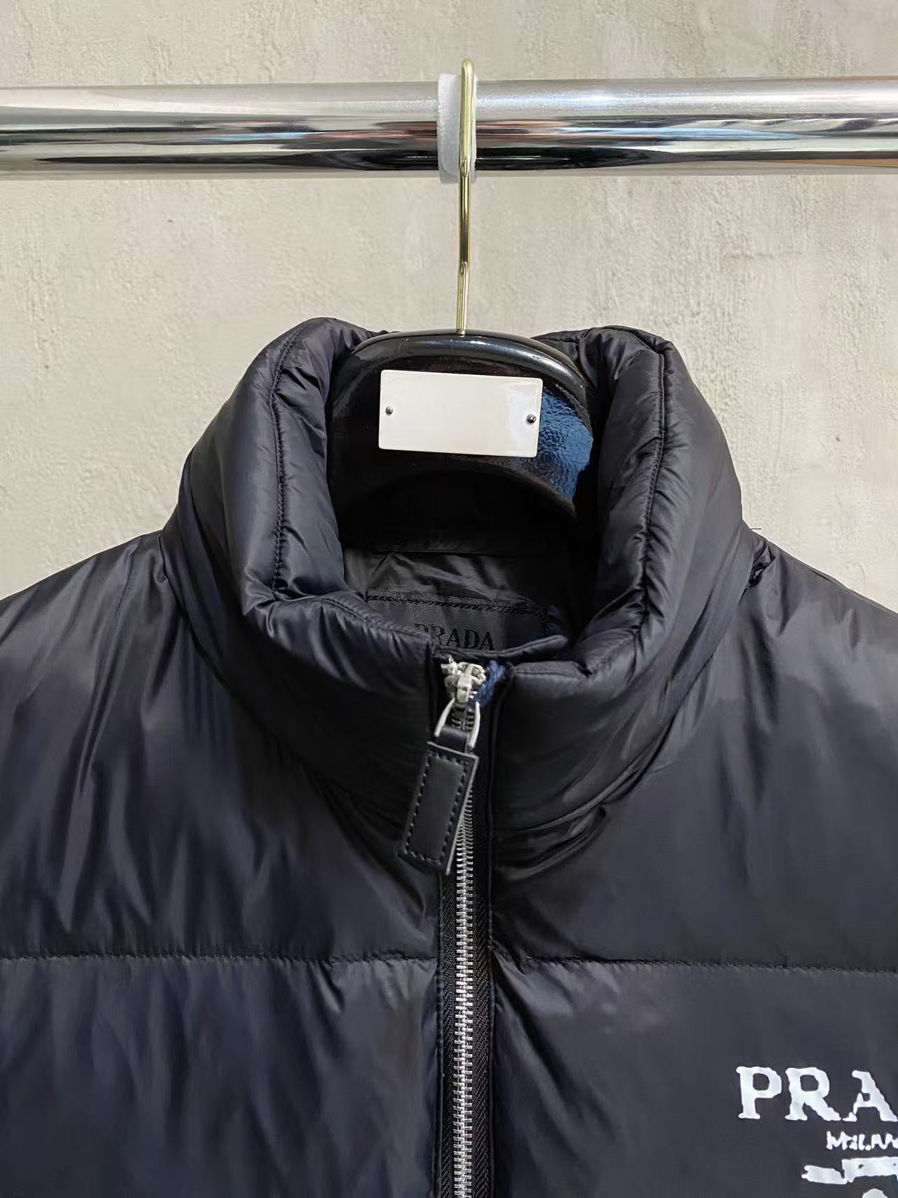 Prada puffer jacket close-up at collar and zipper with logo patch on chest