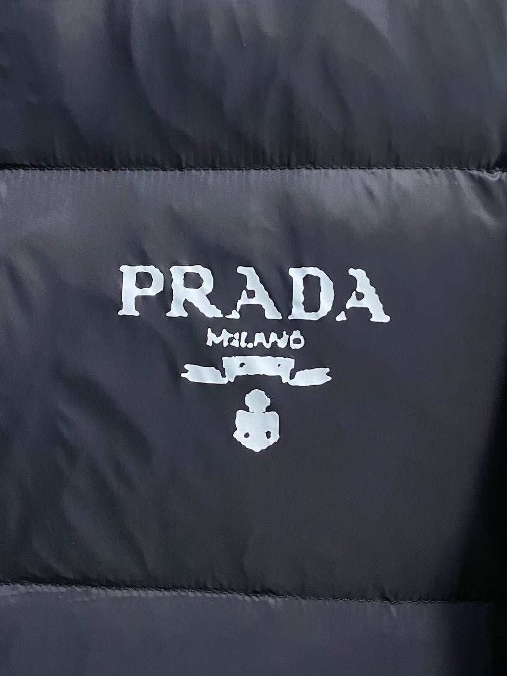 Prada logo on front of puffer jacket, white branding on dark fabric