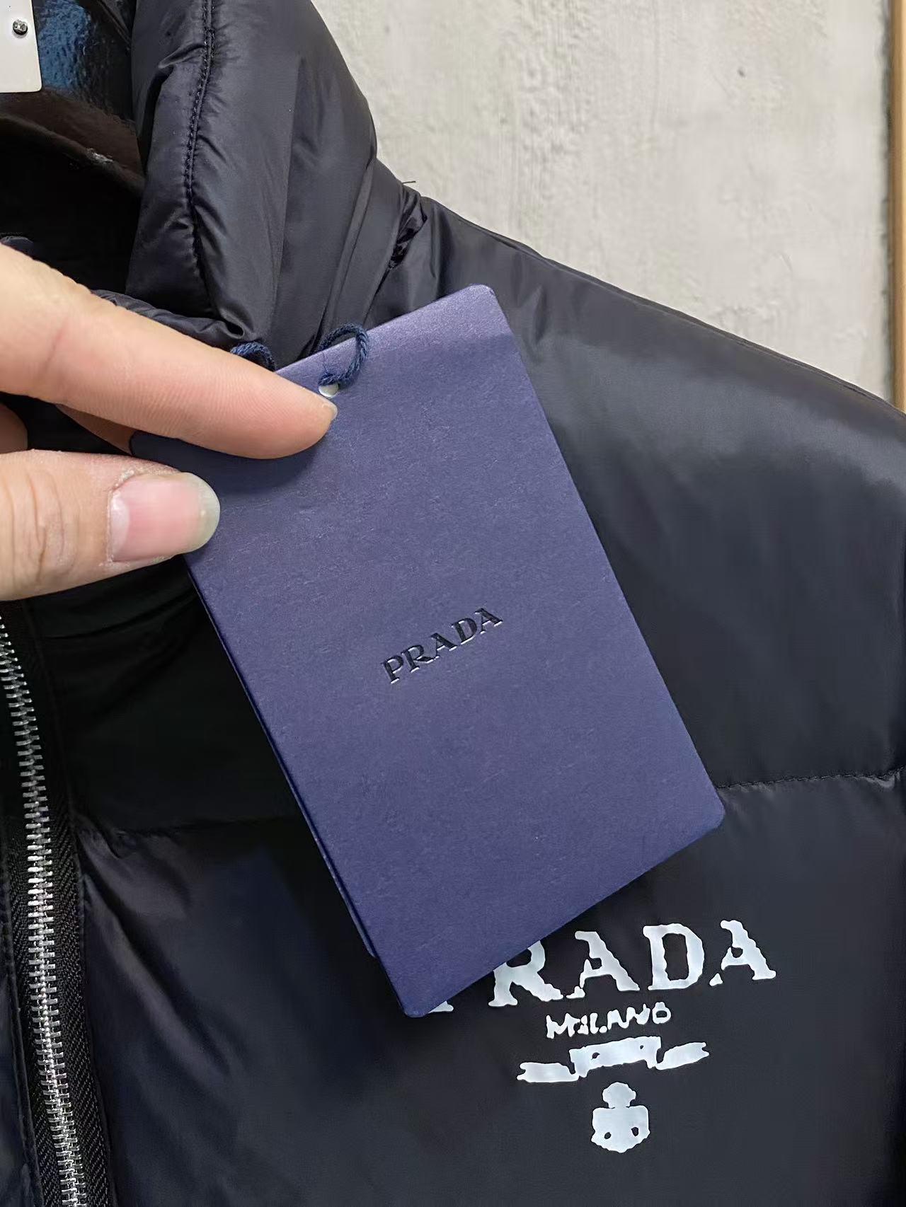 Prada puffer jacket with attached purple garment tag held near chest logo
