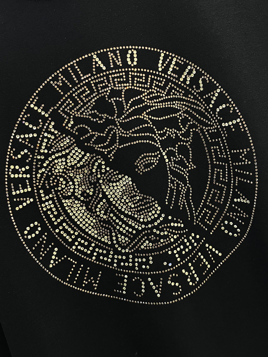 Close-up of black sweatshirt chest emblem with gold studded circular face design