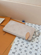 Beige monogram zip pouch with tan pull tab and silver chain wrist strap.