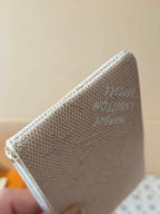 Back corner of a light beige monogram zip pouch with visible embossed logo.