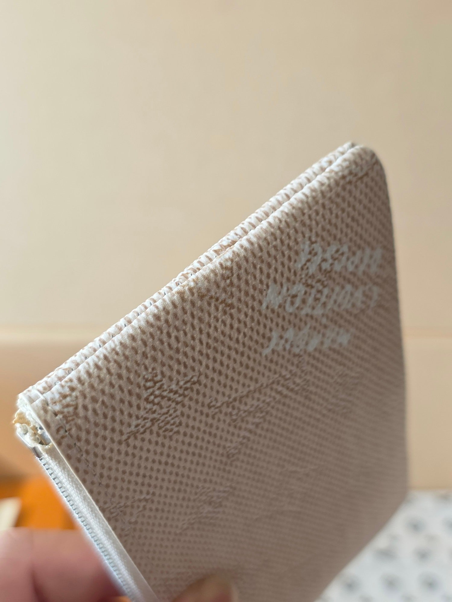 Back corner of a light beige monogram zip pouch with visible embossed logo.
