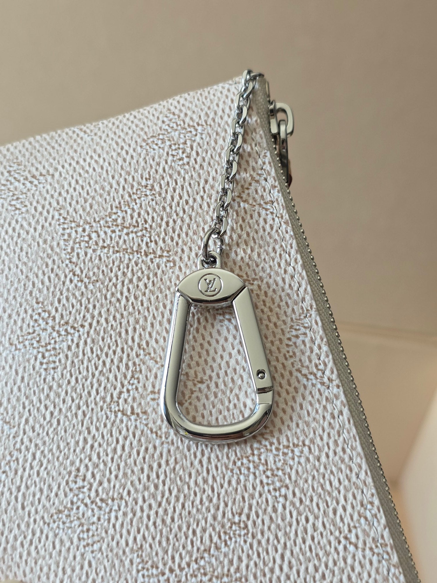 Small zip pouch top view with silver chain and snap hook on textured canvas