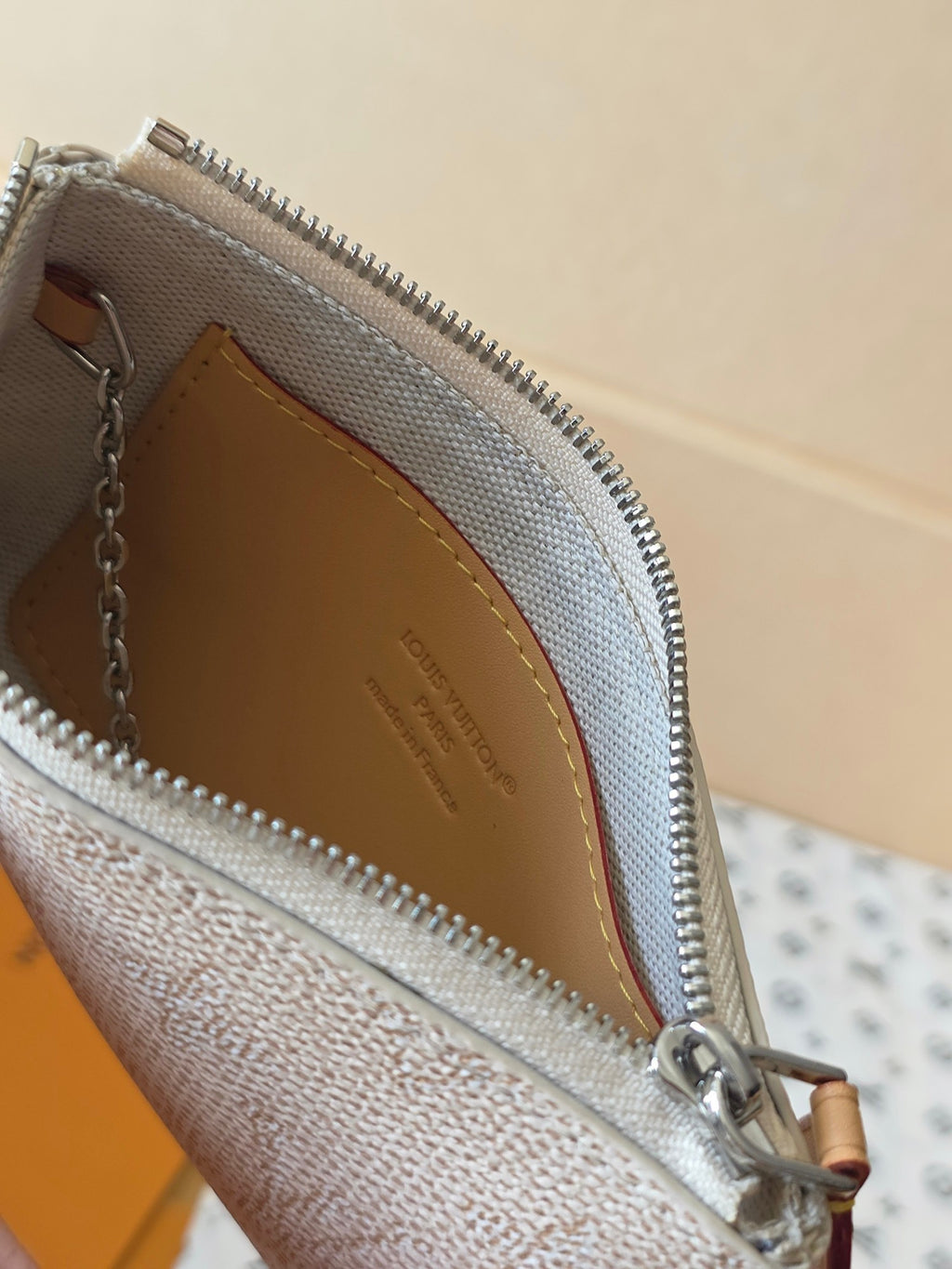 Small zip pouch interior with tan lining, zipper edge, and brand stamp