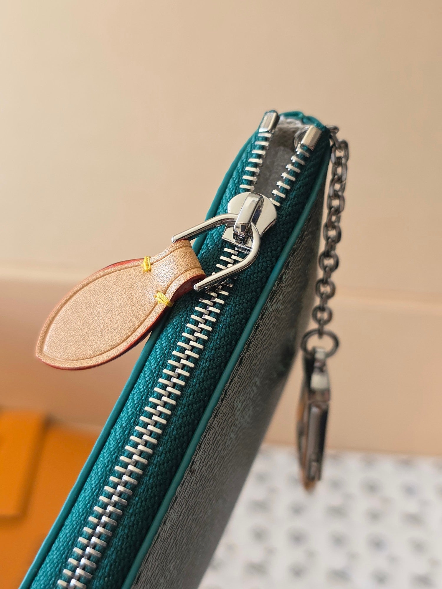 Teal monogram zipper pouch with silver teeth and chain strap, tan leather pull loop