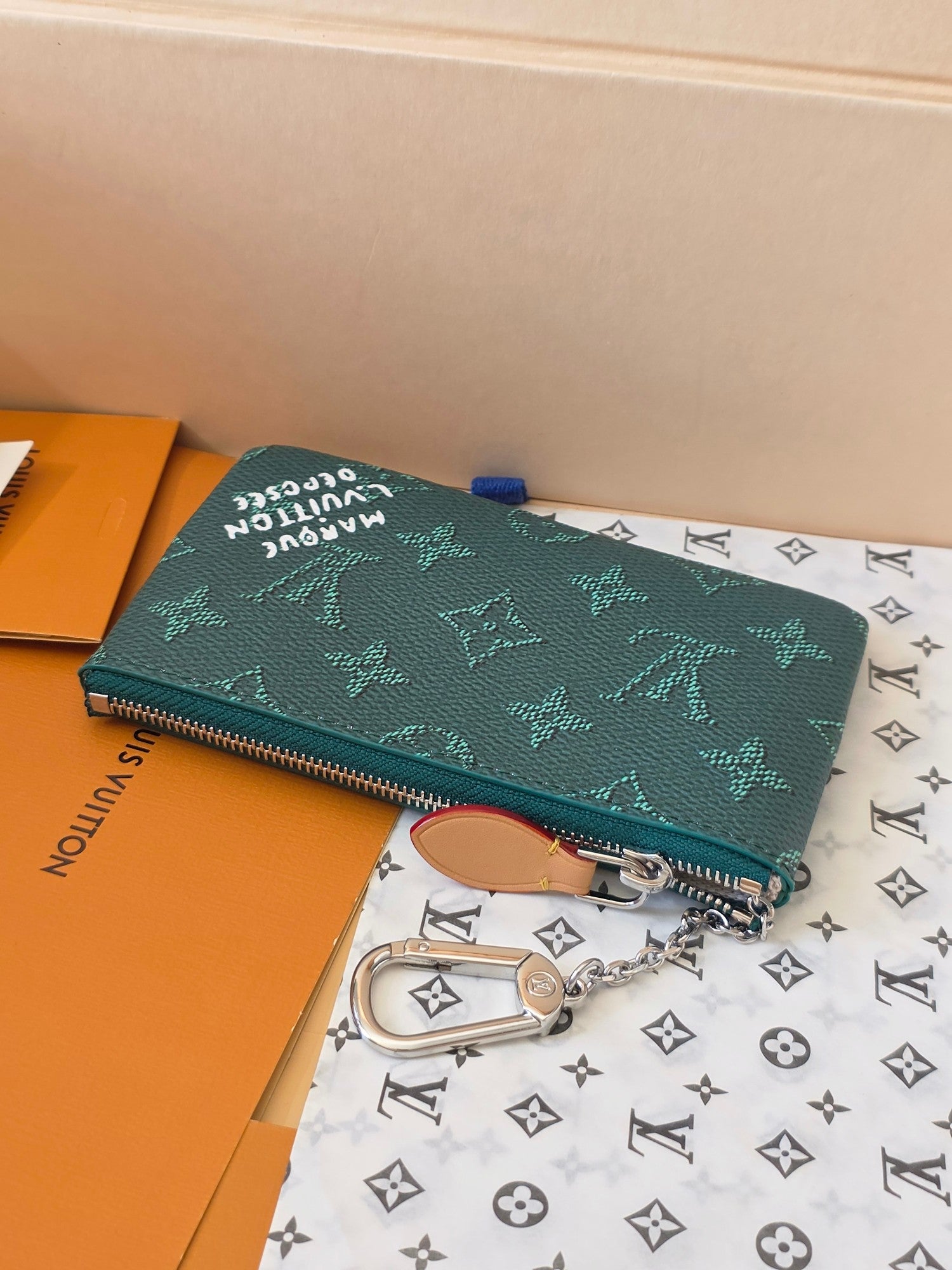 Teal monogram clutch pouch with zipper and silver chain, shown from side angle