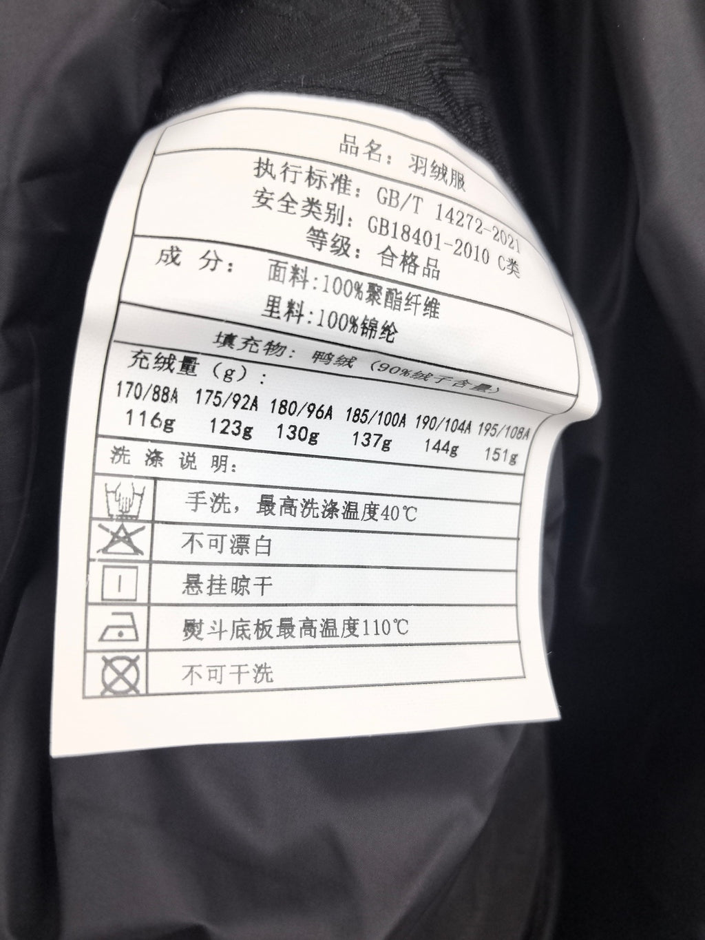 Black jacket care label with materials, wash instructions, and codes