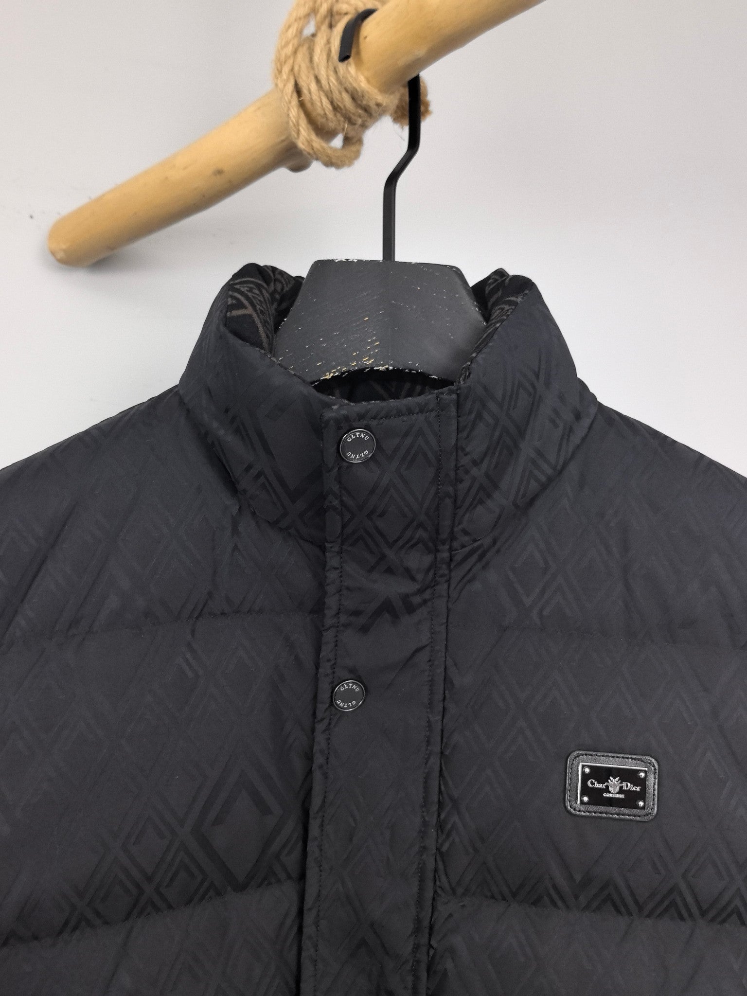 Black puffer jacket close-up: stand collar, front buttons, chest label patch