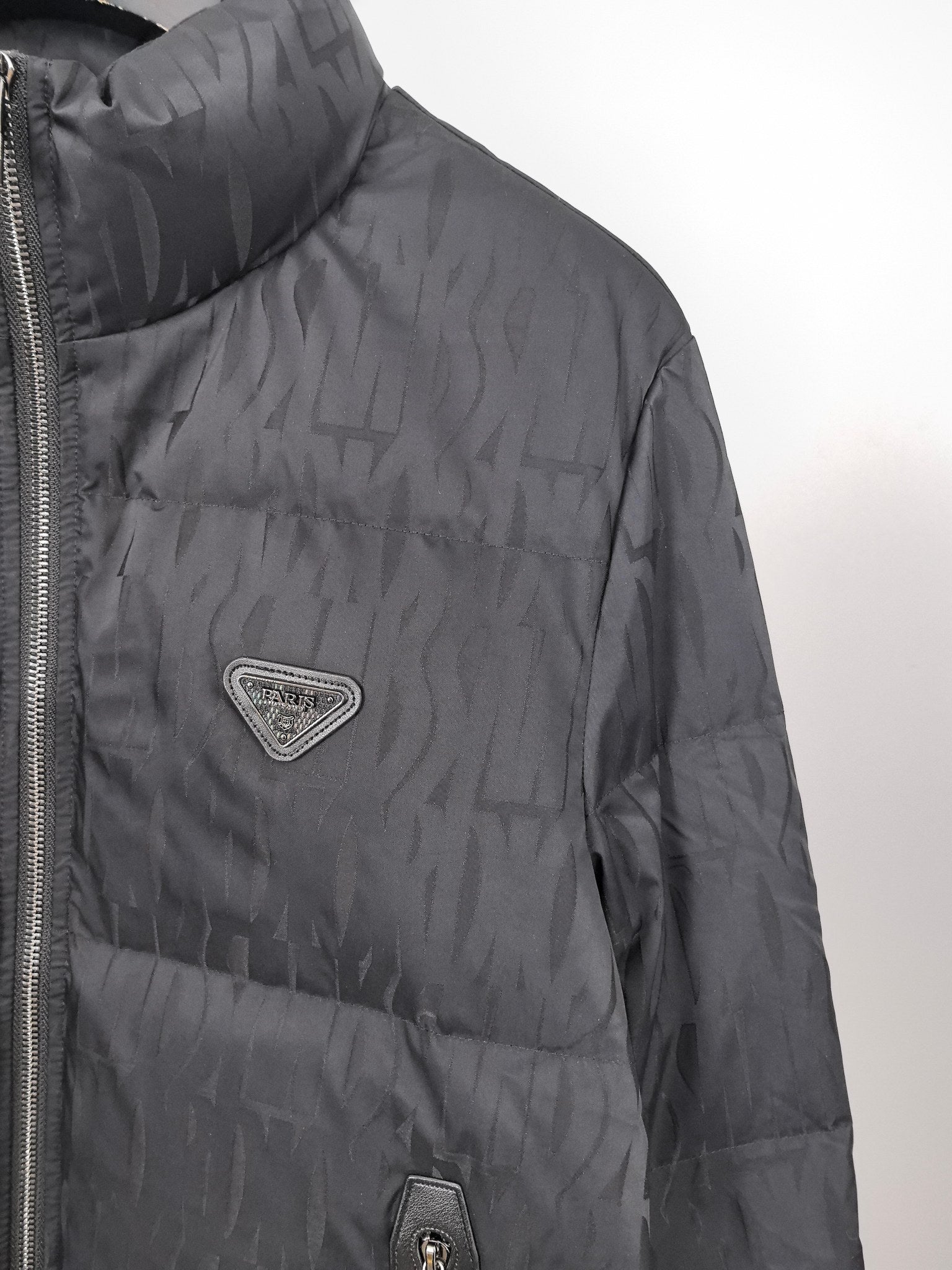 Prada dark puffer jacket close-up with logo patch and side seam zipper