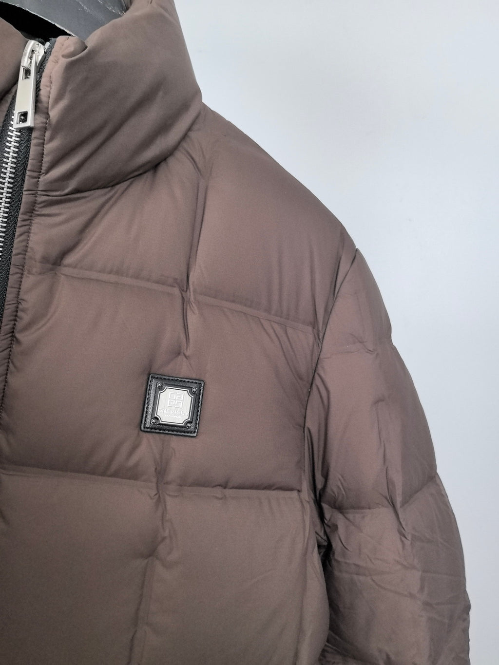 Brown puffer jacket sleeve with square logo patch