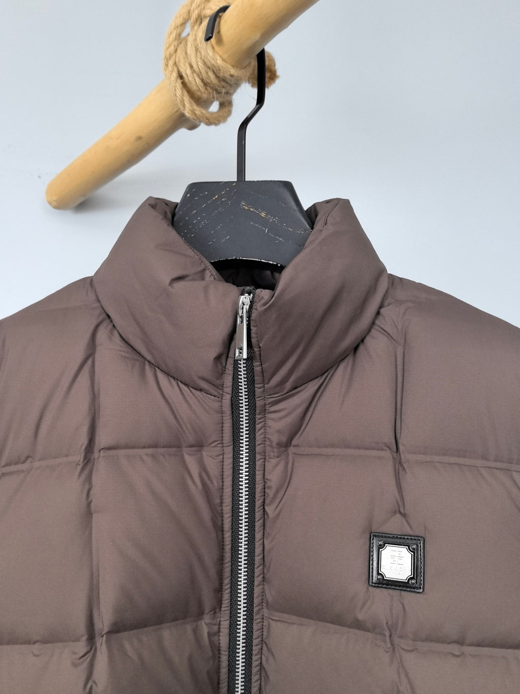 Brown puffer jacket with stand collar, front zipper, and chest logo patch