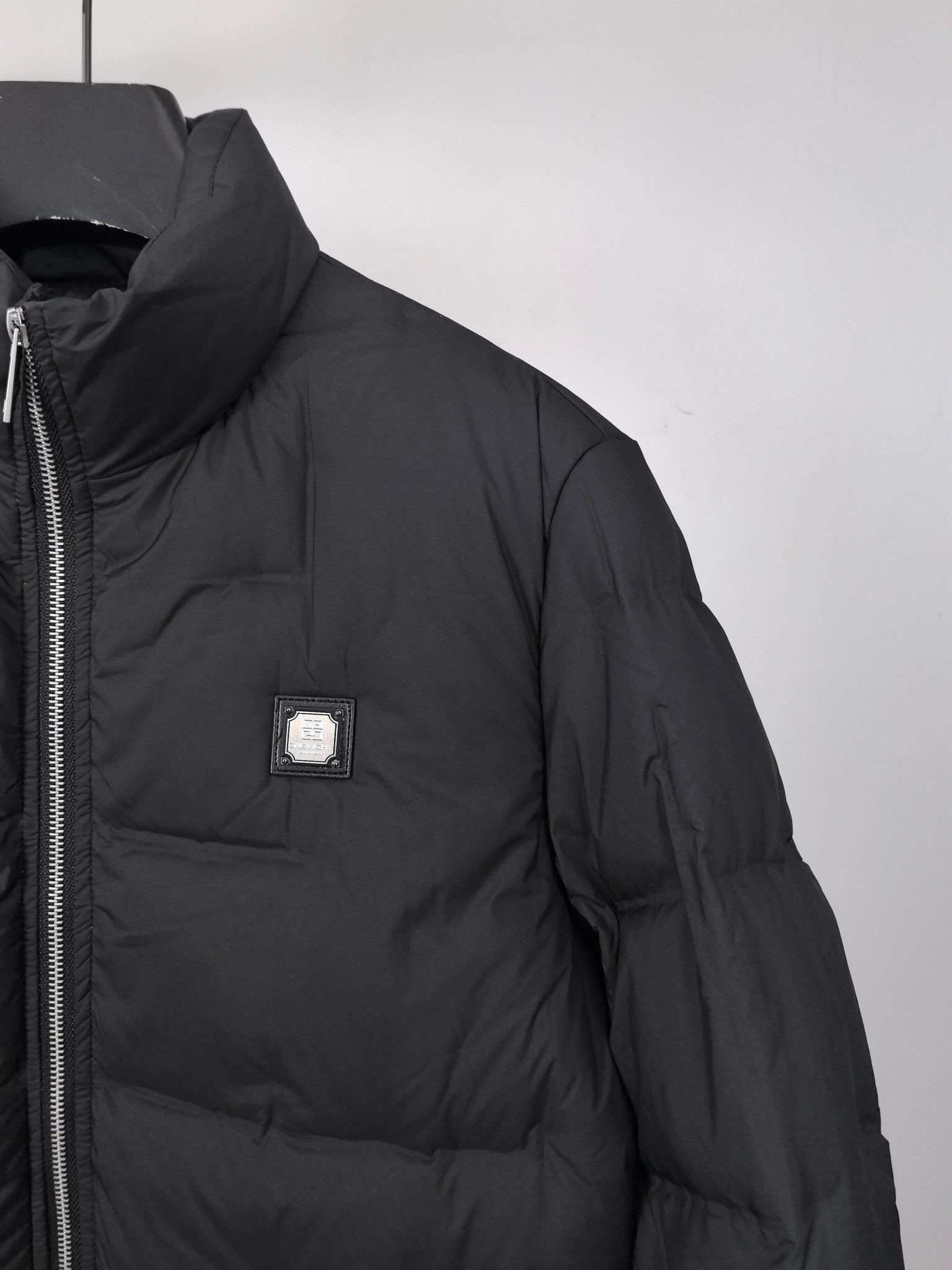 Black puffer jacket side view with chest logo patch and full zipper