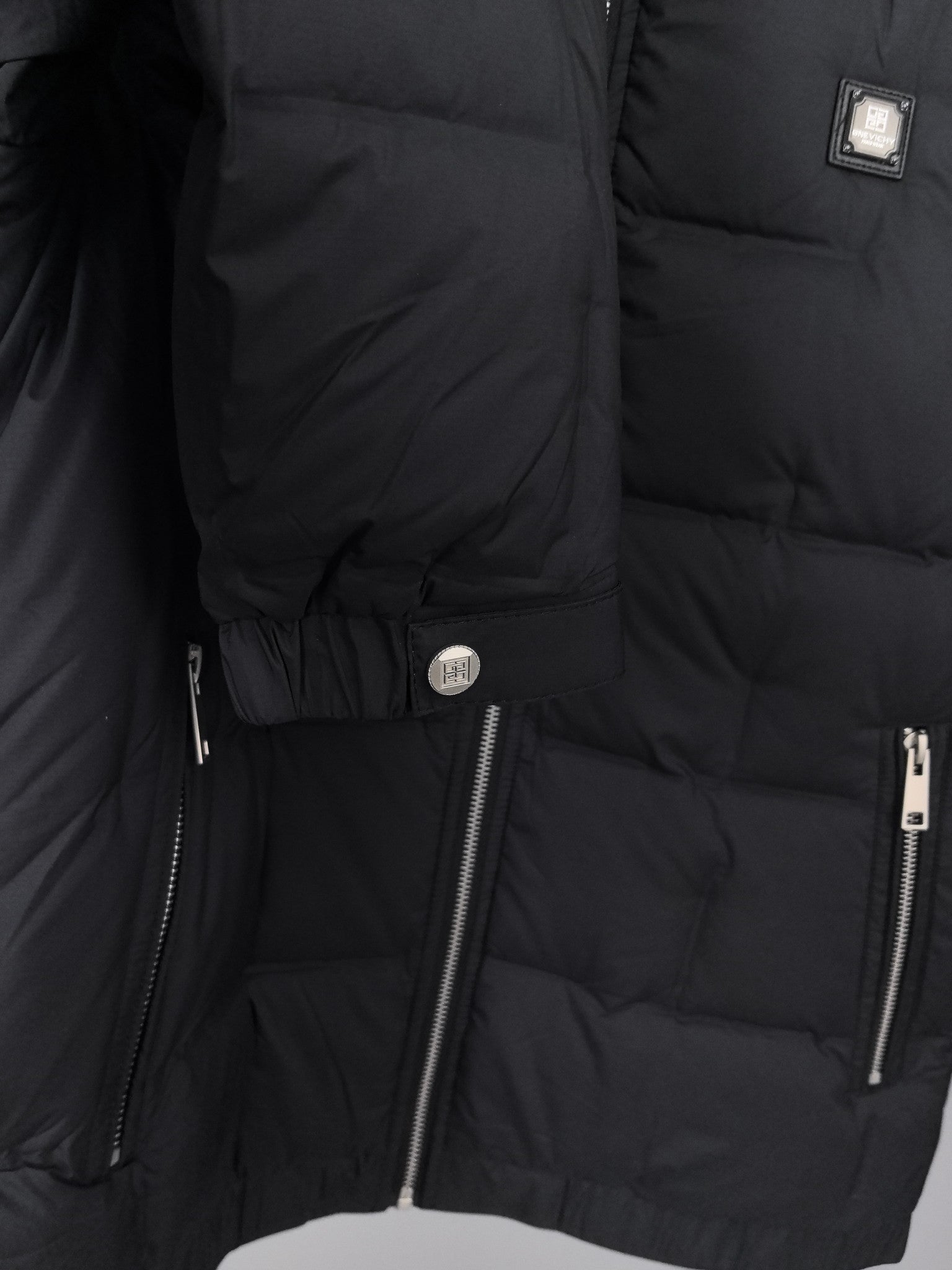 Black puffer jacket close-up of side zip pocket and logo pull tab