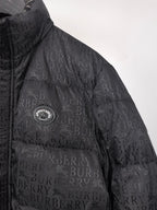 Long black puffer jacket with circular chest emblem and repeating Burberry pattern