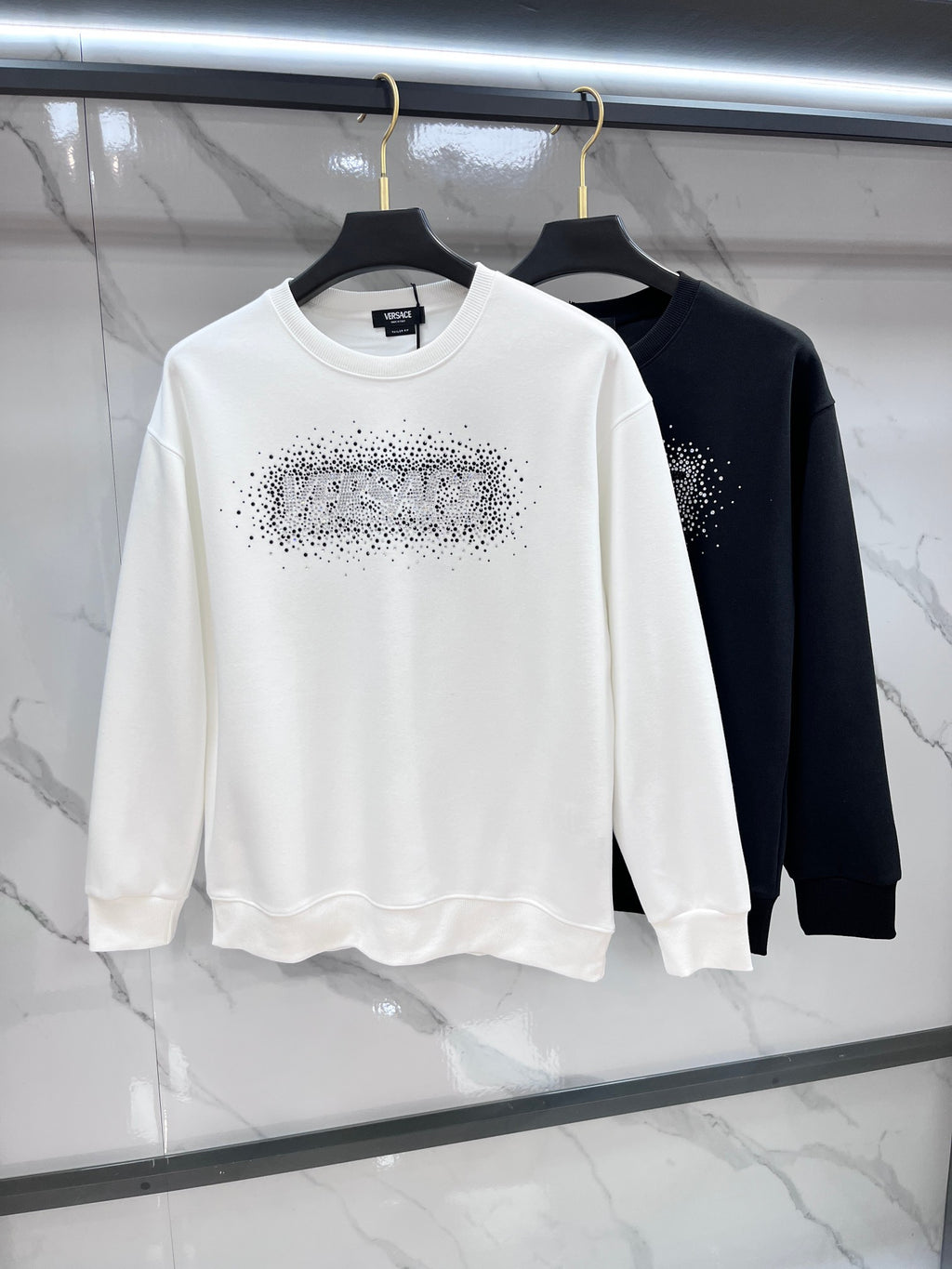 White and black crewneck sweatshirts with rhinestone logos on the chests