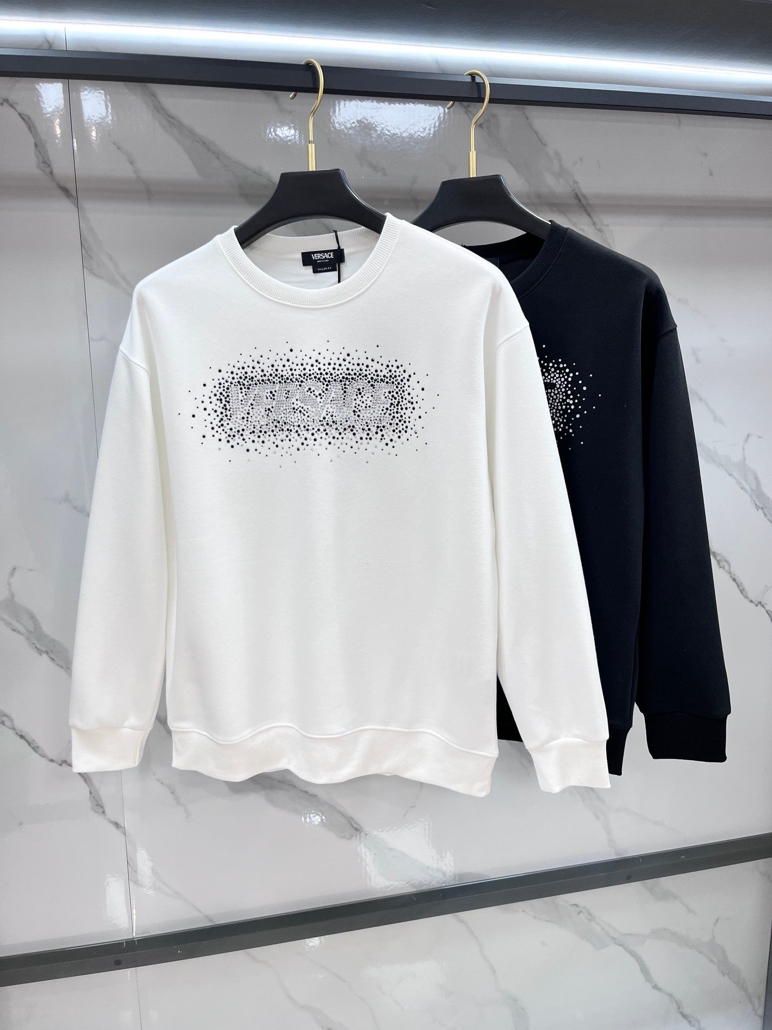 White and black crewneck sweatshirts with rhinestone logos on the chests