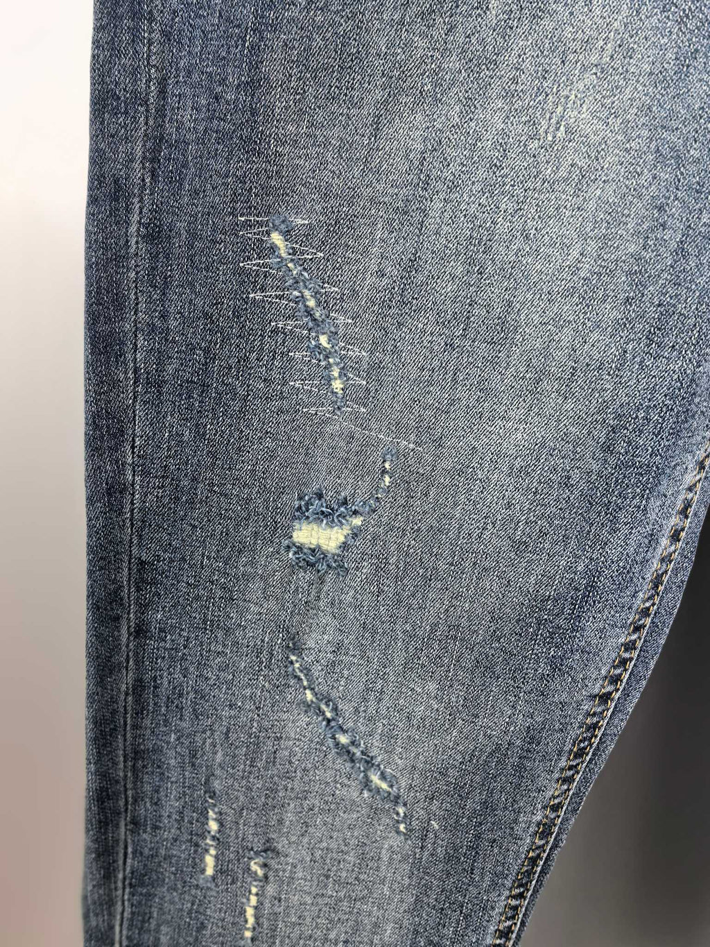 Denim pants leg with distressed yellow patch and visible hand-stitching