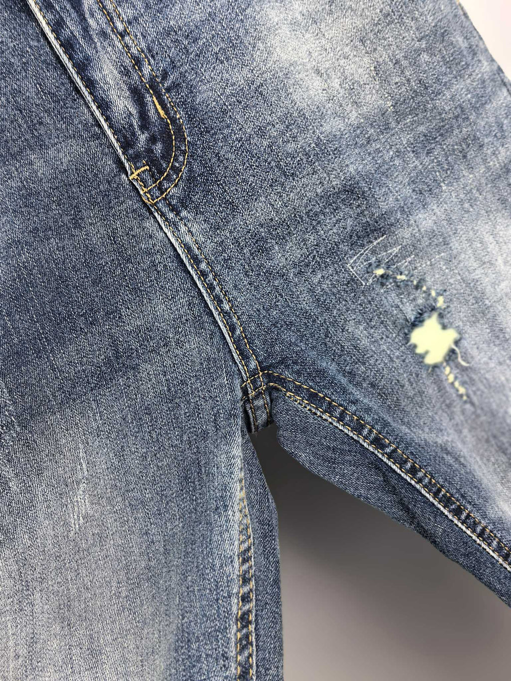 Denim pants side seam with distressed opening and small yellow repair patch