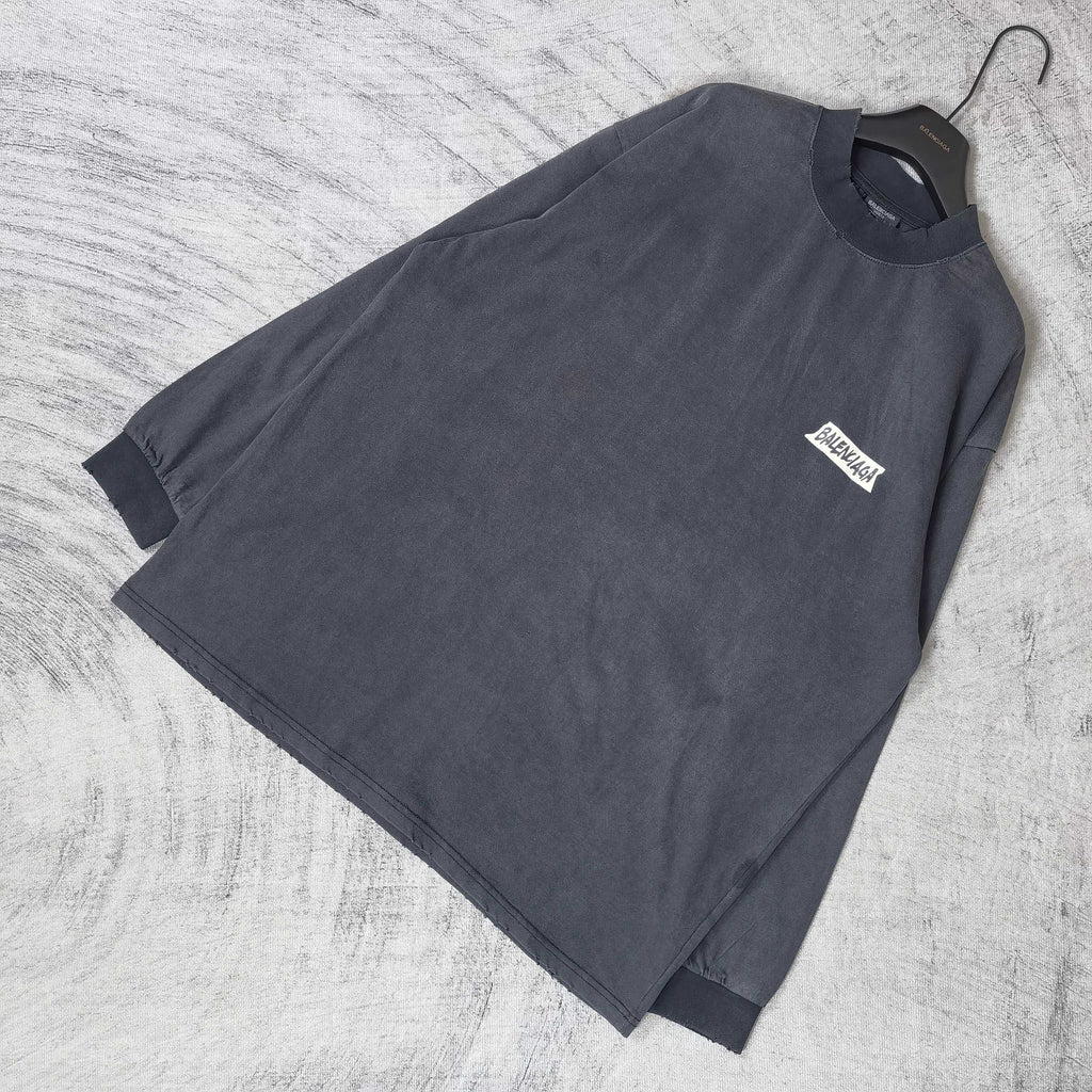 Balenciaga long-sleeve top laid flat, dark charcoal gray, small chest logo patch