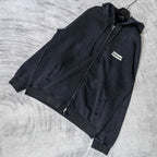 Black hoodie jacket, laid out at angle, with front zipper and logo patch