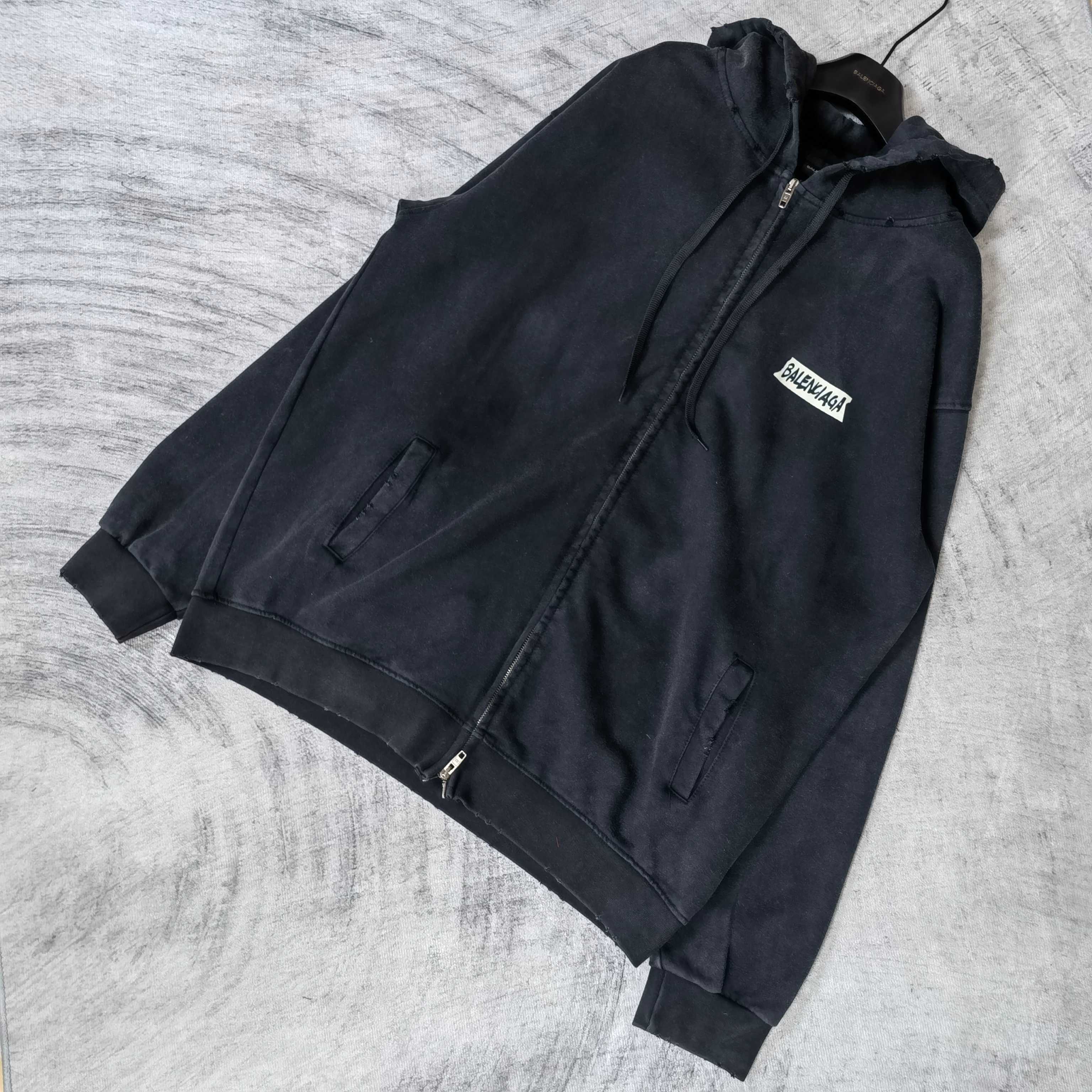 Black hoodie jacket, laid out at angle, with front zipper and logo patch