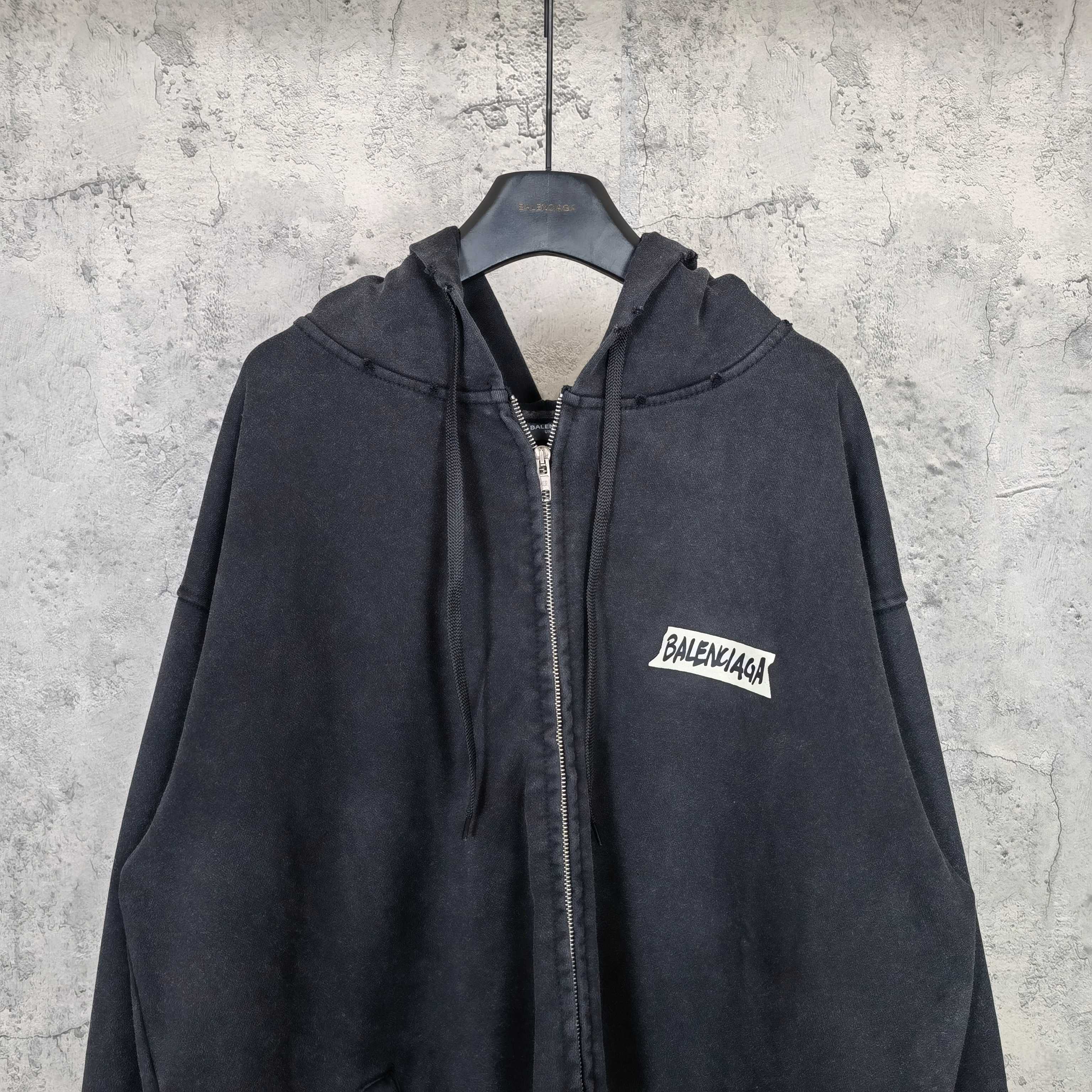 Black zip-up hoodie with hood, front zipper, and chest logo patch