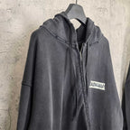 Black zip-up hoodie jacket with hood, front zipper, and chest logo patch