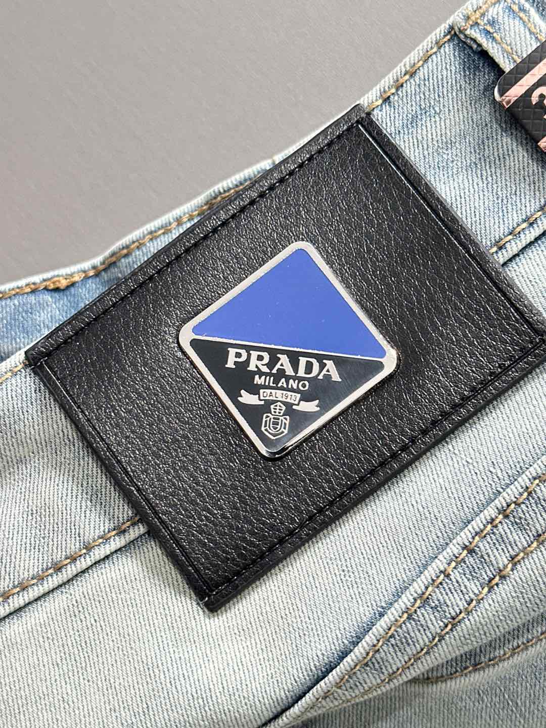 Black leather brand patch with PRADA logo on light-wash denim pocket
