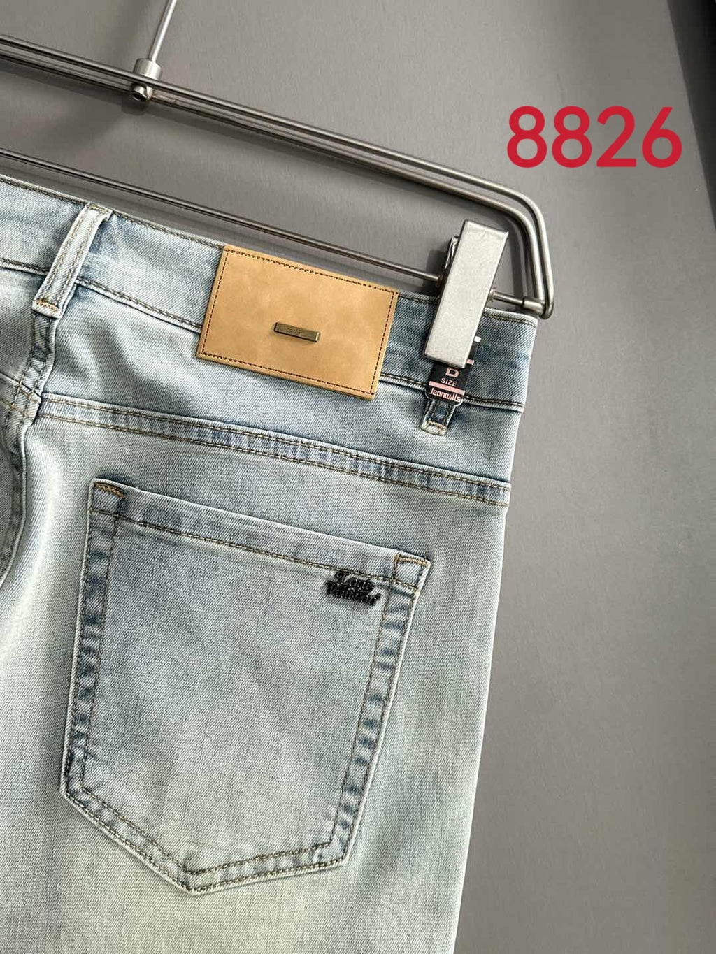 Light wash denim pants back pocket with tan leather logo patch and metal rivets
