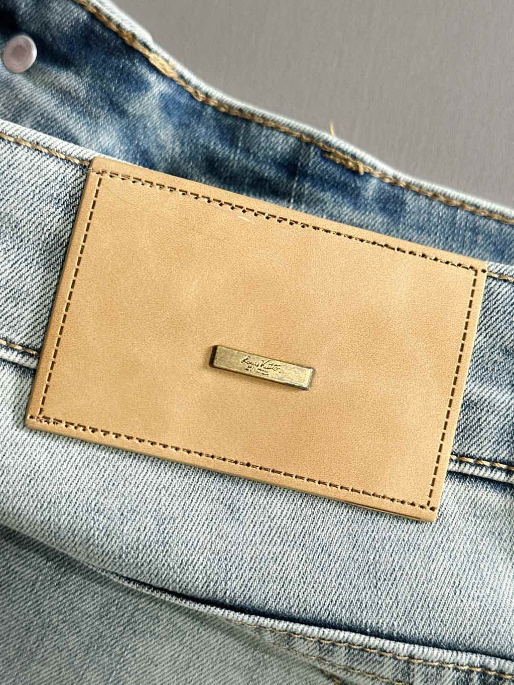 Light wash denim pants waistband with tan leather logo patch and stitch border