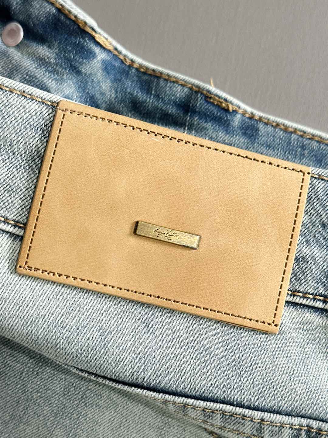 Light wash denim pants waistband with tan leather logo patch and stitch border