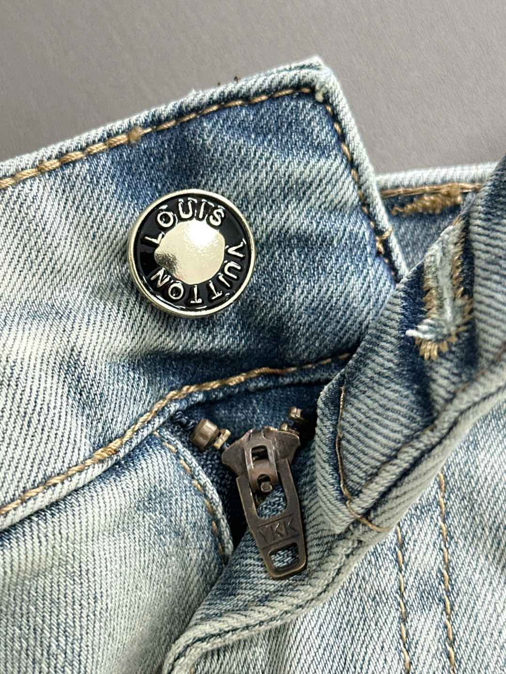 Light wash denim pants with round metal logo button and riveted fly