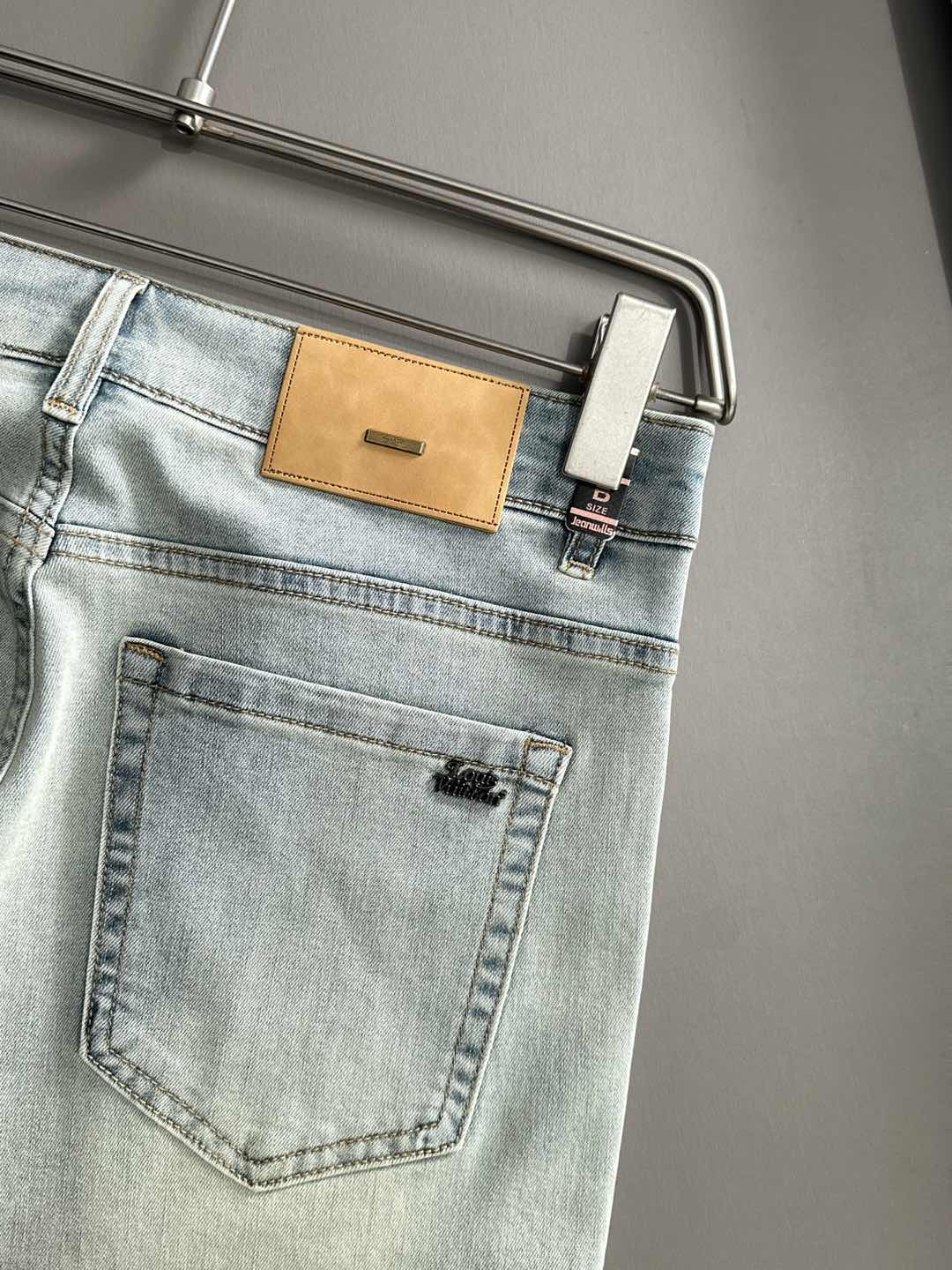 Light wash denim pants back pocket and tan leather logo patch close-up