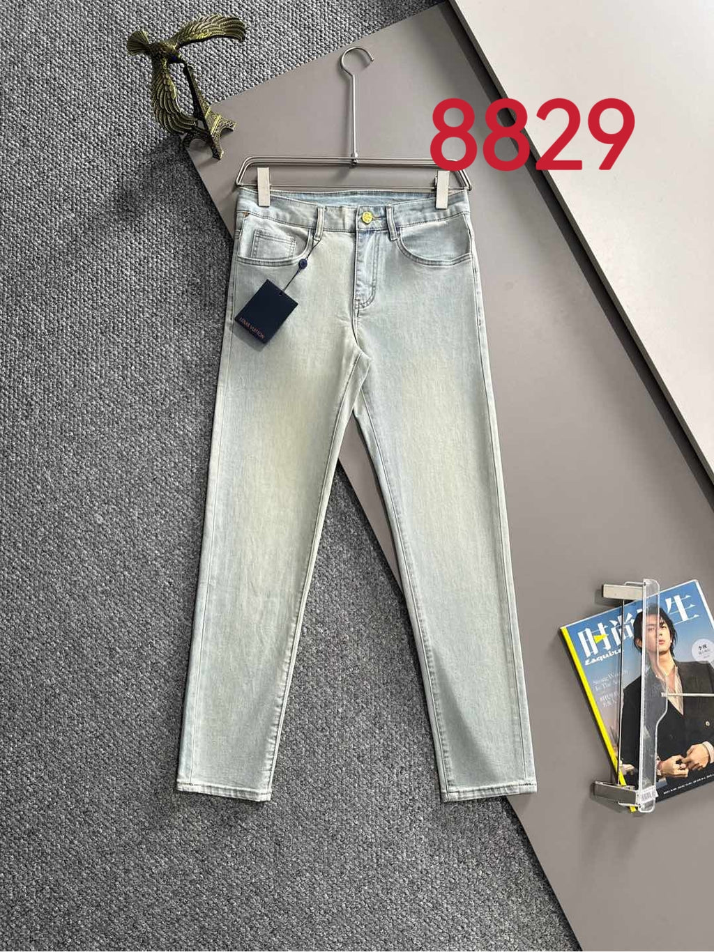 Light-wash denim jeans with front pockets and visible designer button, hung on a hanger