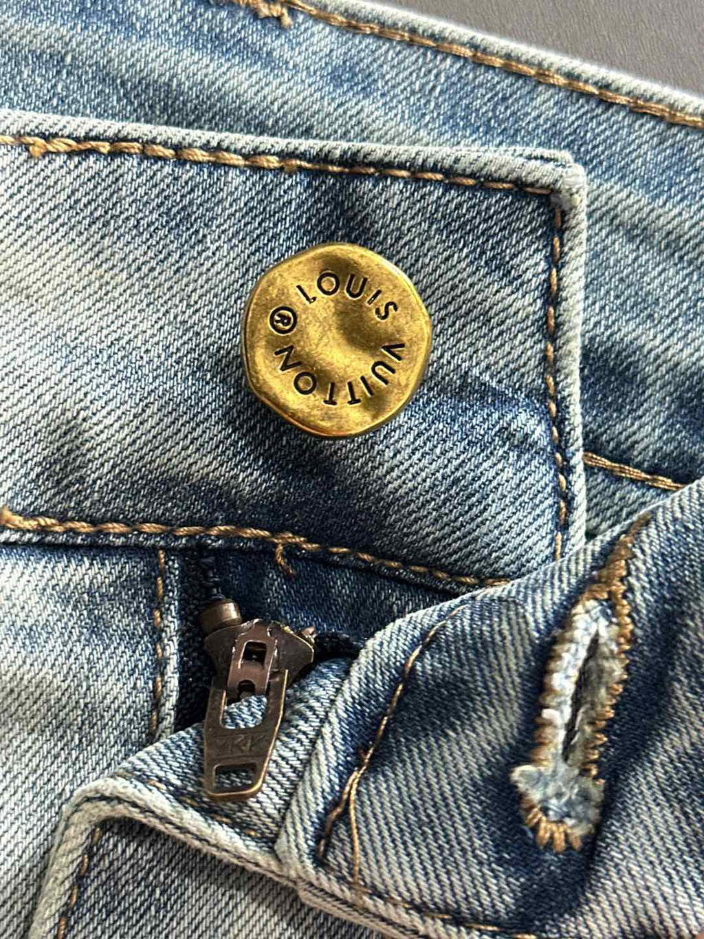 Light-wash denim jeans close-up of gold button with LV logo