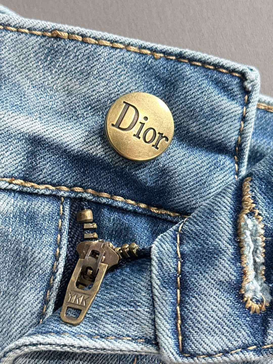 Dior gold button on light blue denim pocket with visible stitching