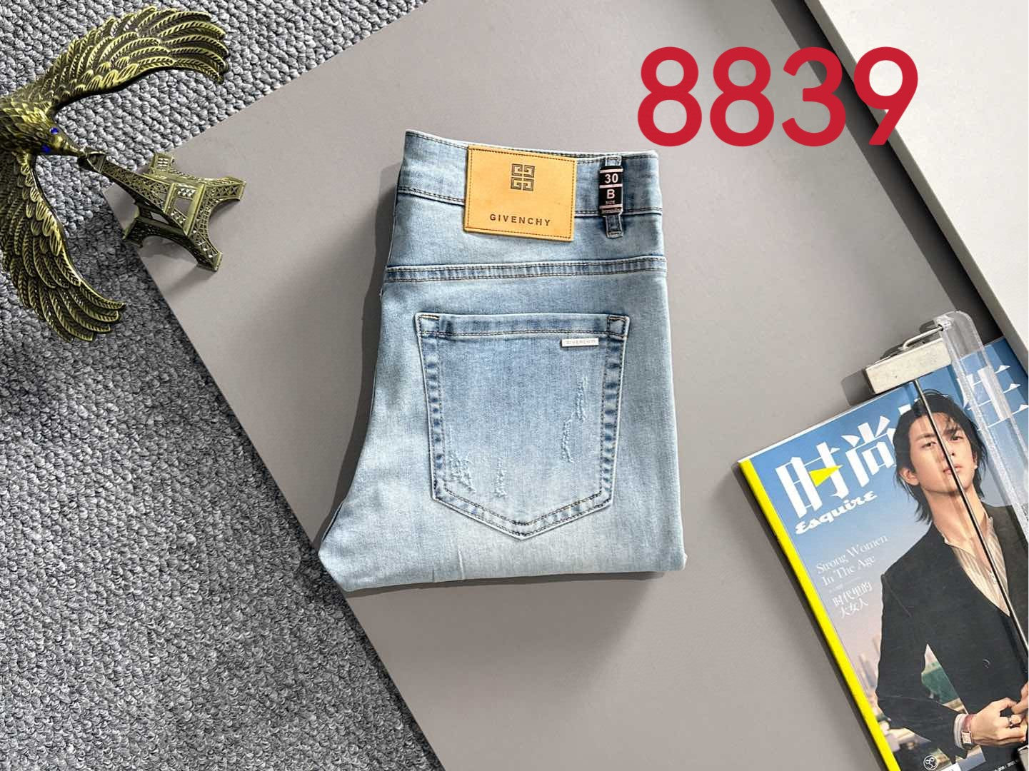Light blue denim jeans folded flat with orange GIVENCHY logo patch and tag.