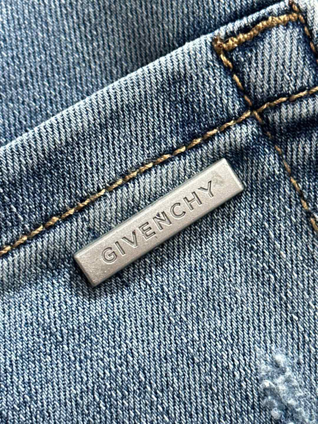 GIVENCHY metal logo tag on light blue denim with contrast stitching.