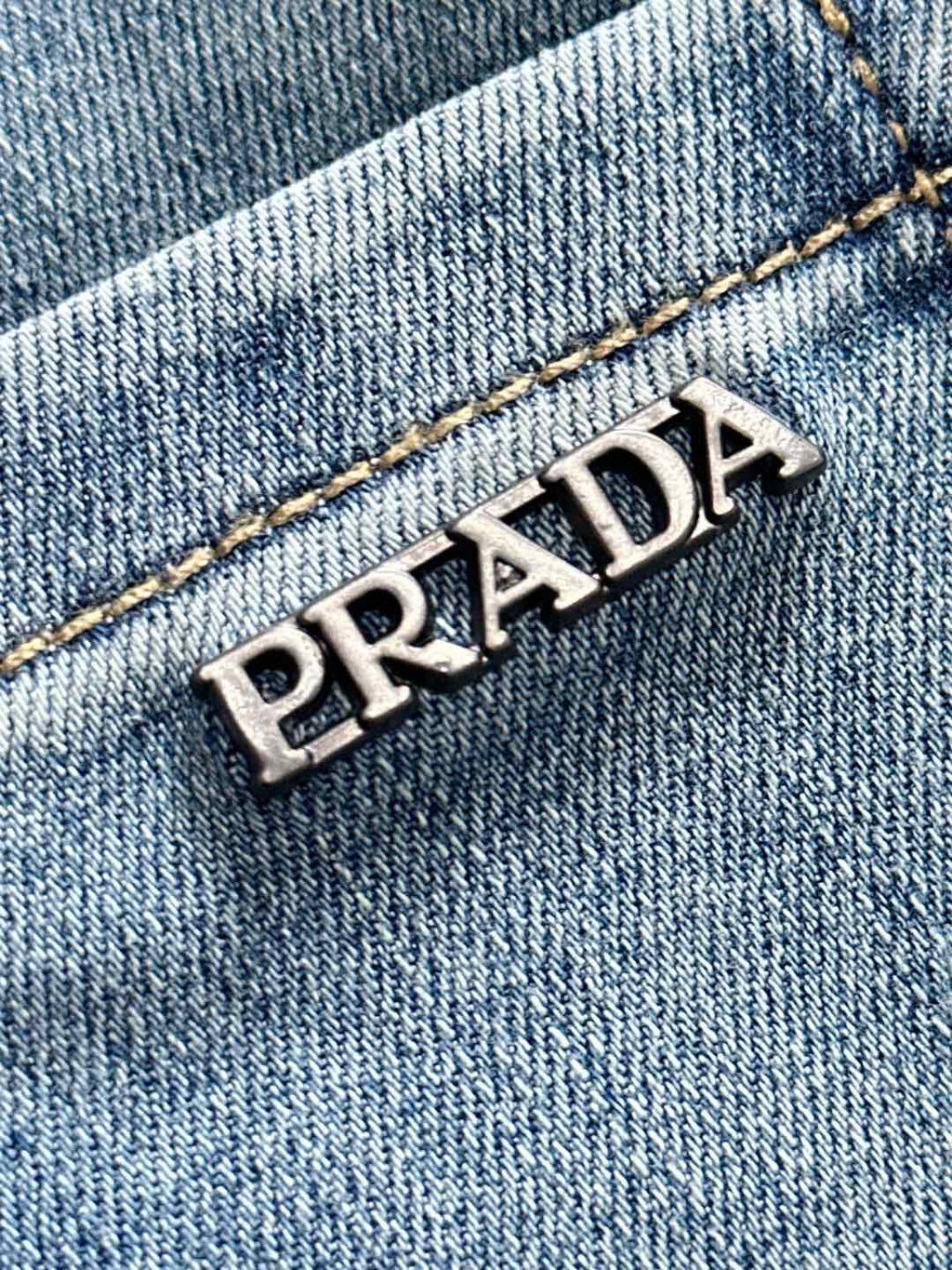 PRADA logo patch on light blue denim, embroidered detail close-up.