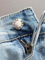 PRADA engraved metal jeans button and zip fly close-up on denim.