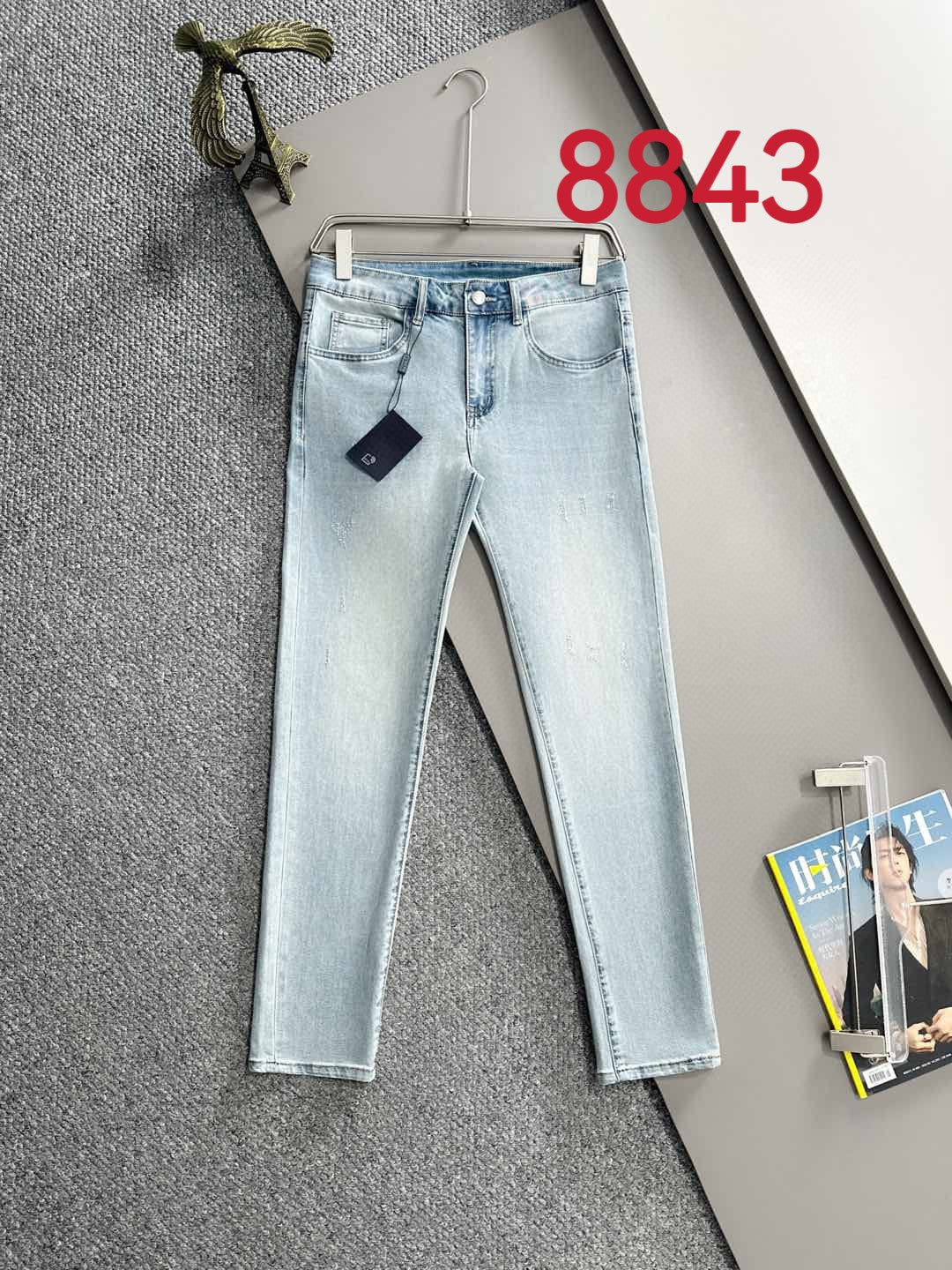 Light blue denim pants on hanger with straight legs and five-pocket design.