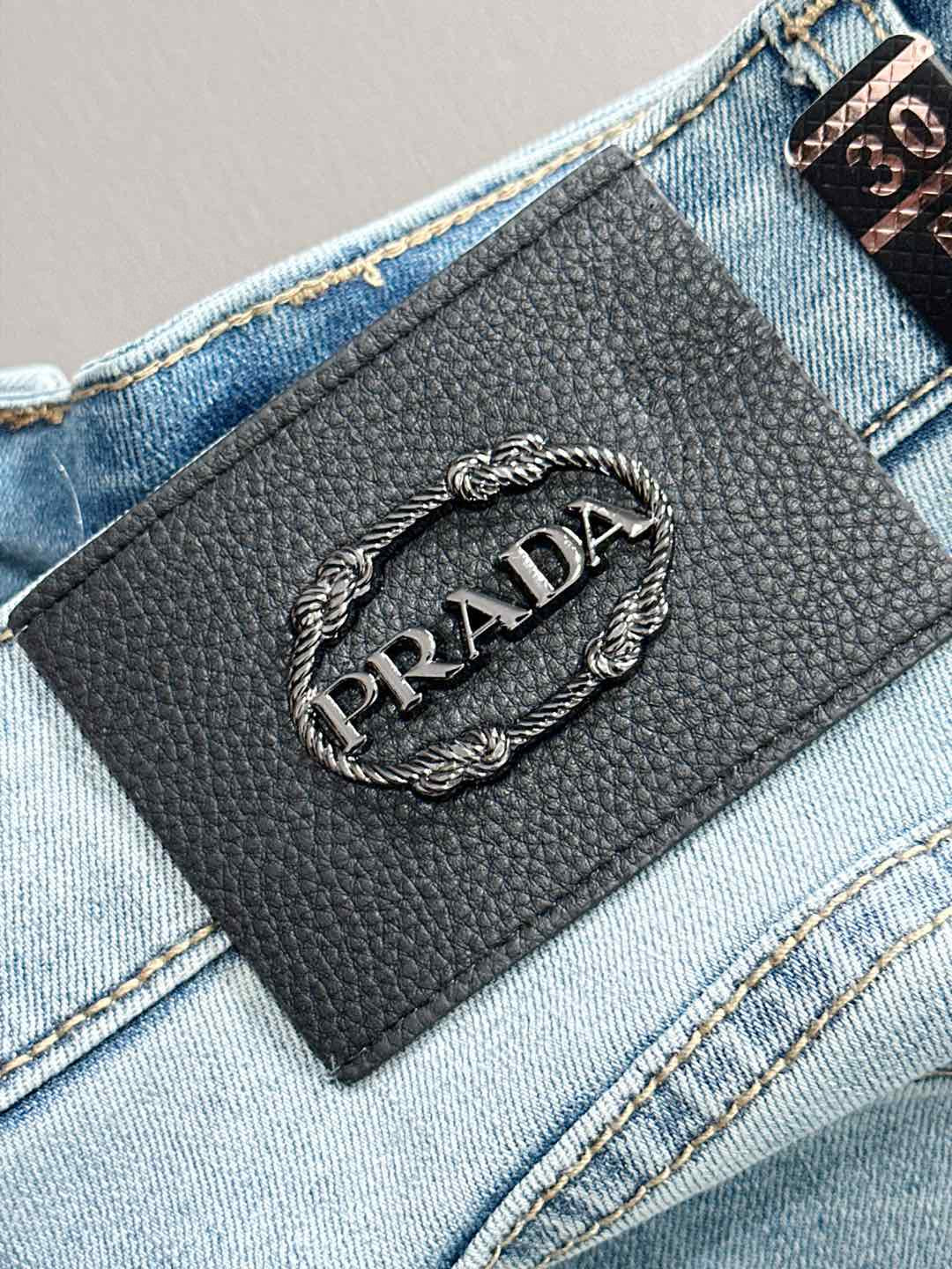 Black leather Prada logo label on light blue denim pants near waistband.