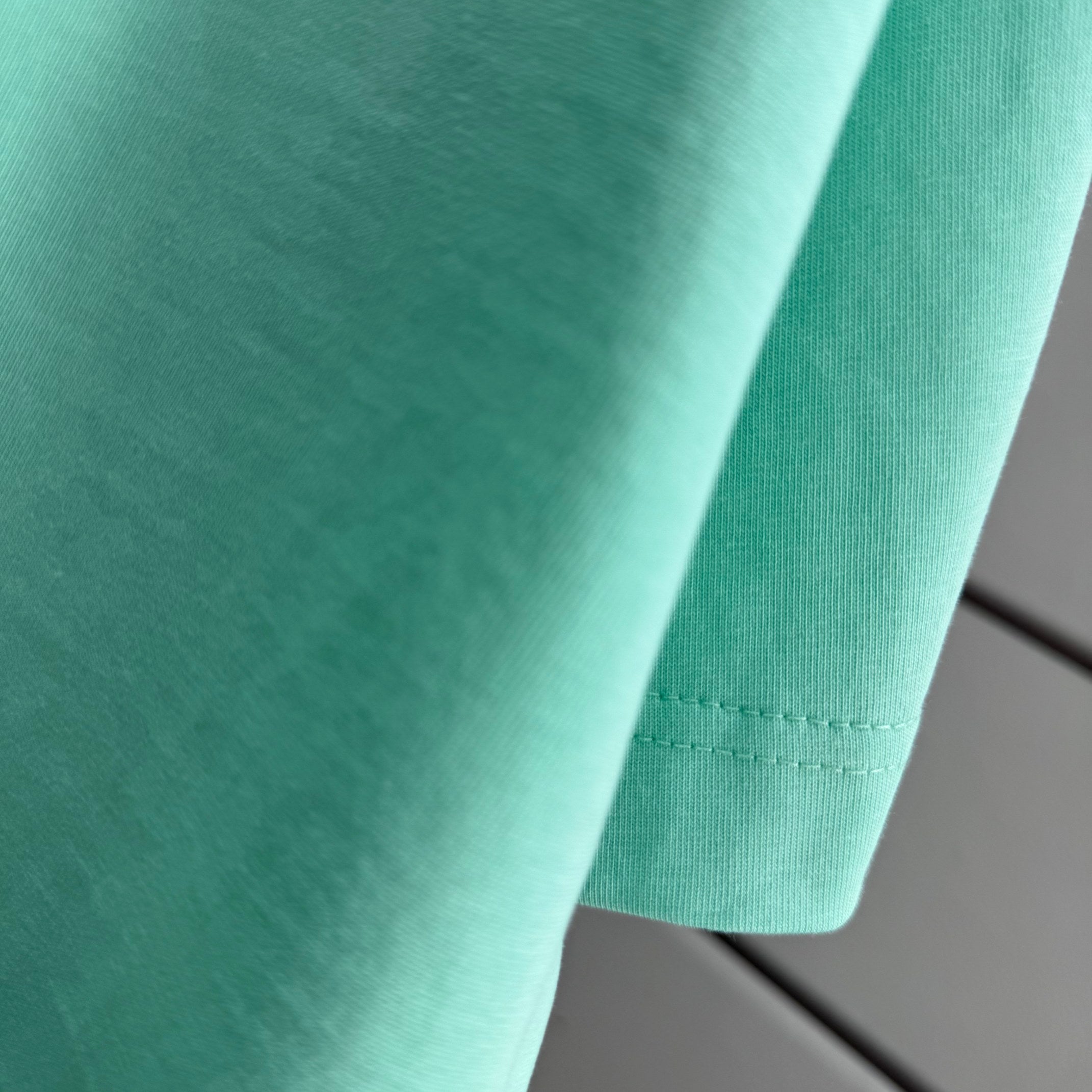 Mint green Burberry T-shirt fabric close-up with stitched hem