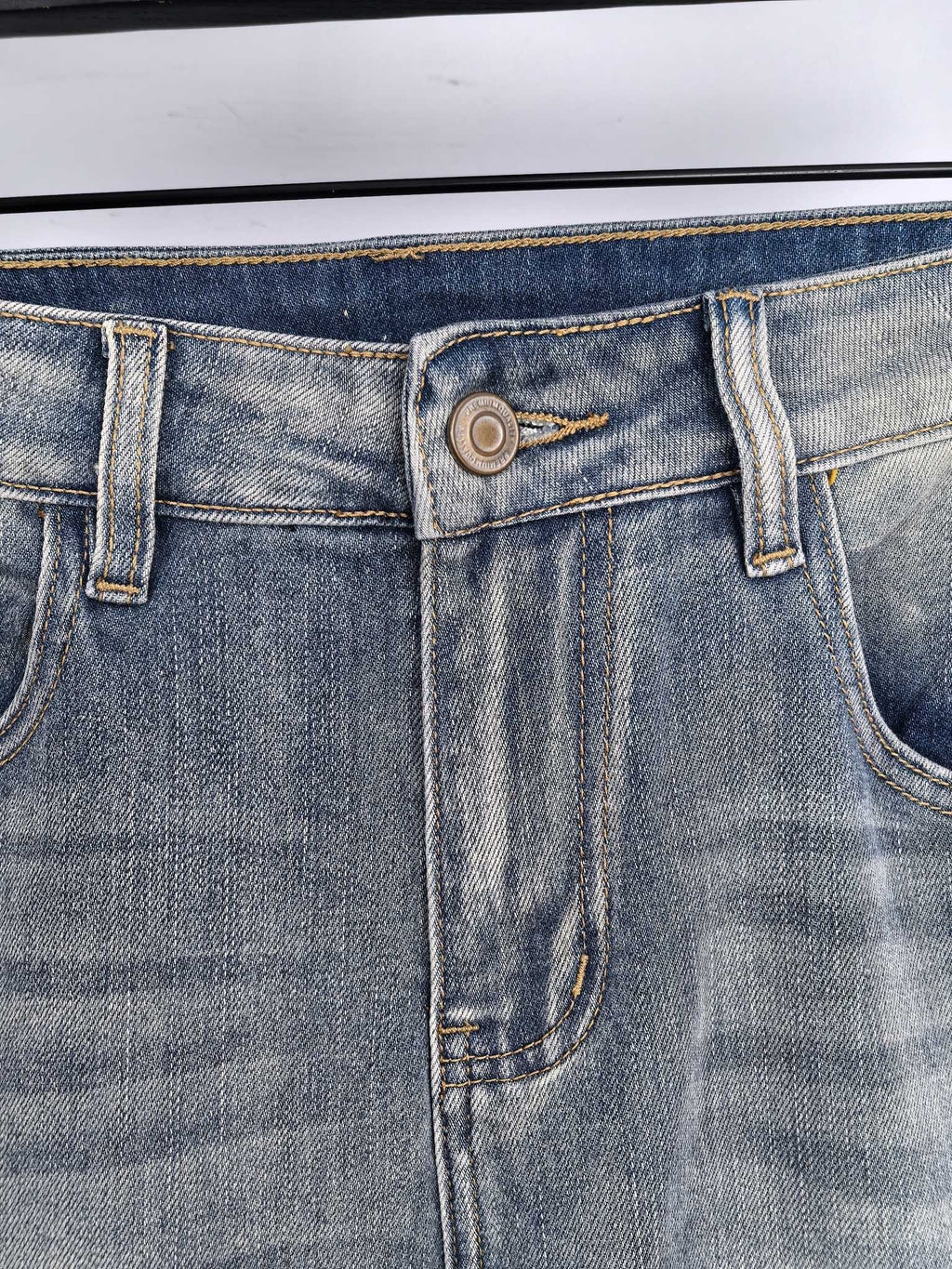 Back-pocket and waistband detail on light wash denim jeans, with stitched seams