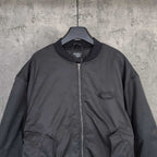 Dark bomber jacket front with stand collar, zip closure, and oval logo patch