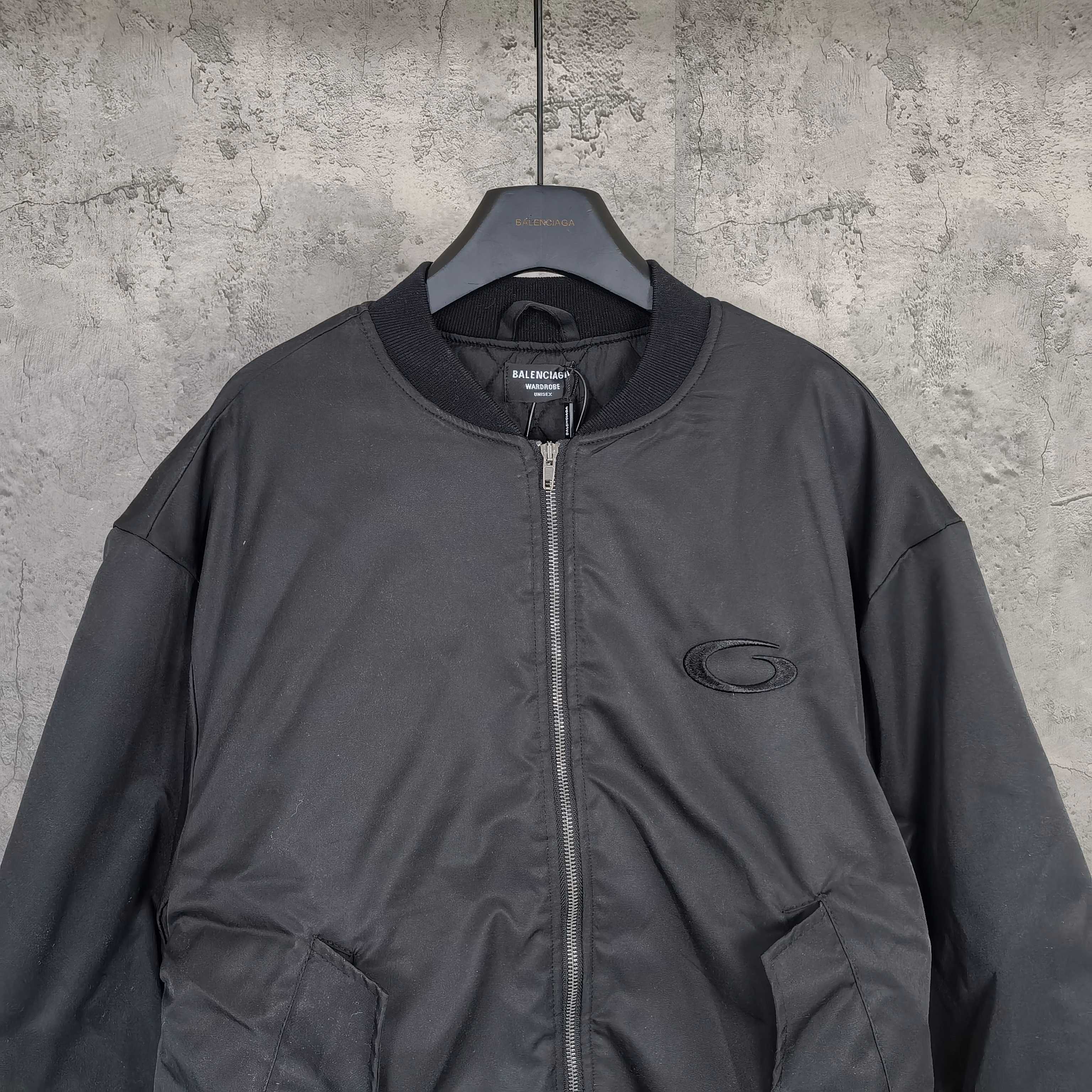 Dark bomber jacket front with stand collar, zip closure, and oval logo patch