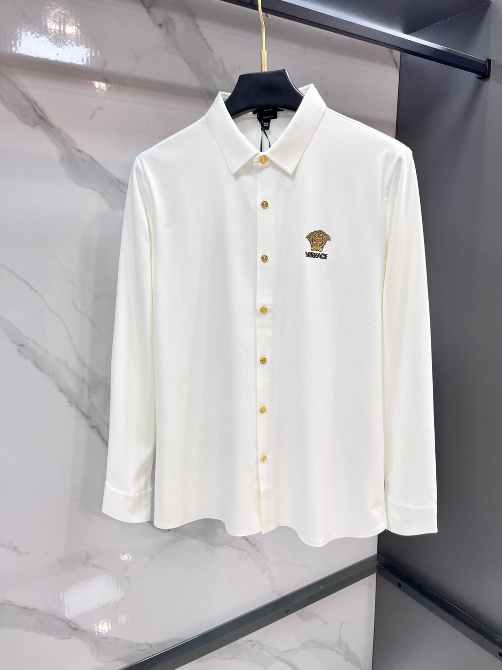 White long-sleeve button-up shirt with gold buttons and small chest logo crest